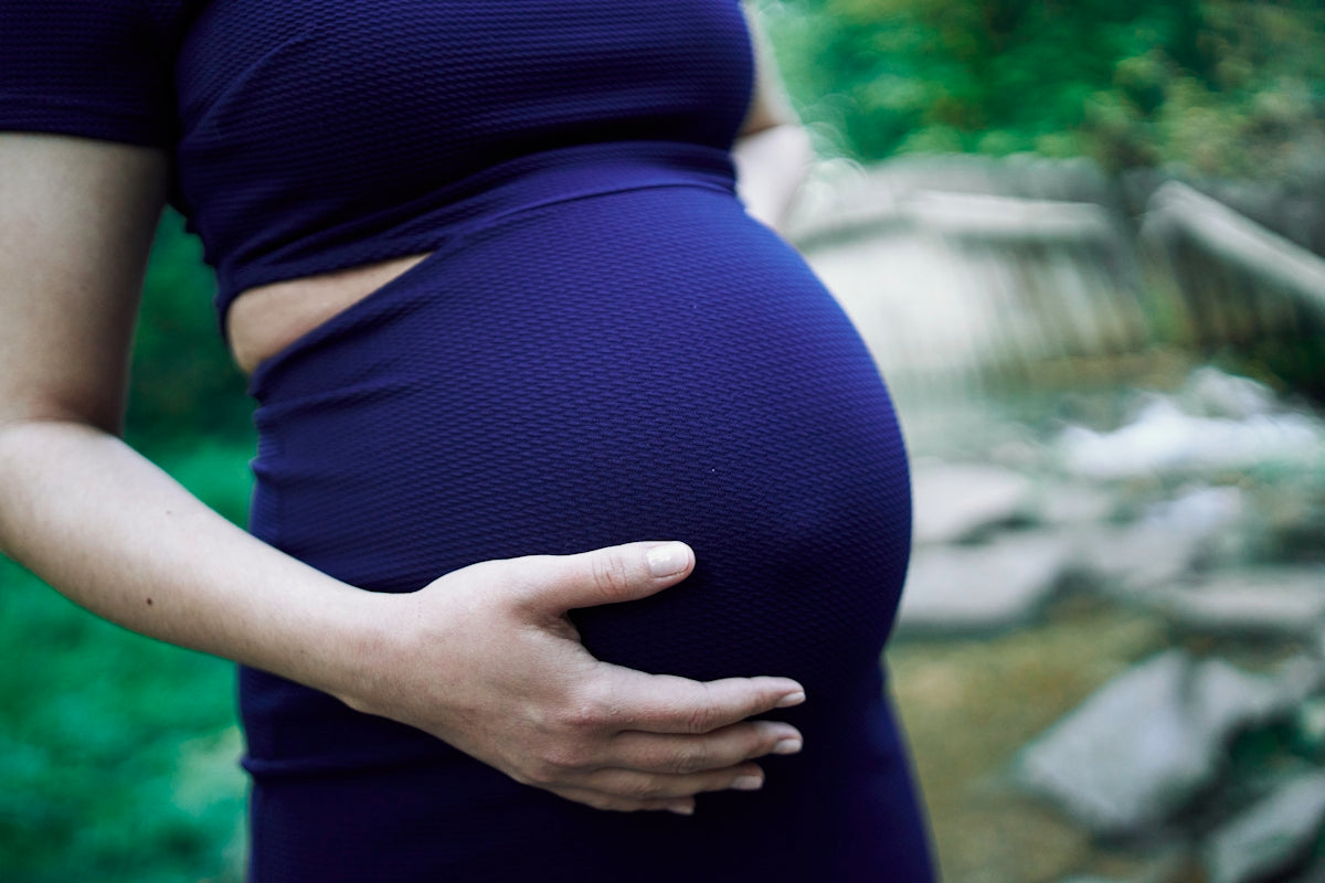 a pregnant woman in a blue dress holding her belly
