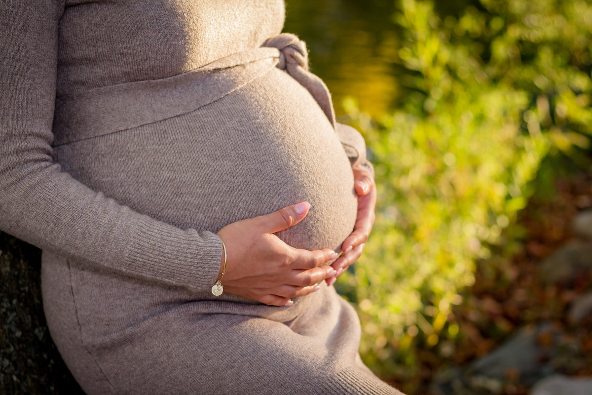 pregnant woman wearing gray long-sleeved dress touching her tummy while standing